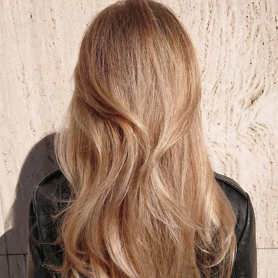 A person facing a speckled gray wall. They have long, golden honey blonde hair