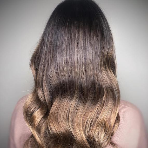 Back of woman’s head with wavy dark hon-ey hair, created using Wella Professionals.
