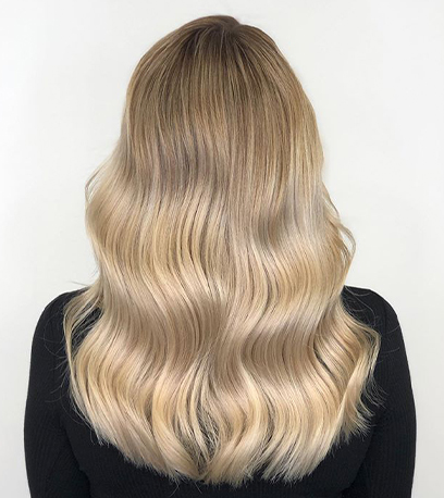 Model with long, wavy, blonde hair and pearlescent Illuminage, created using Wella Professionals.