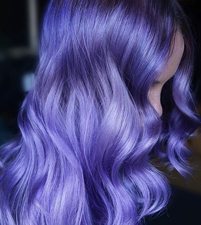 Side profile of a person with wavy, bright lilac hair